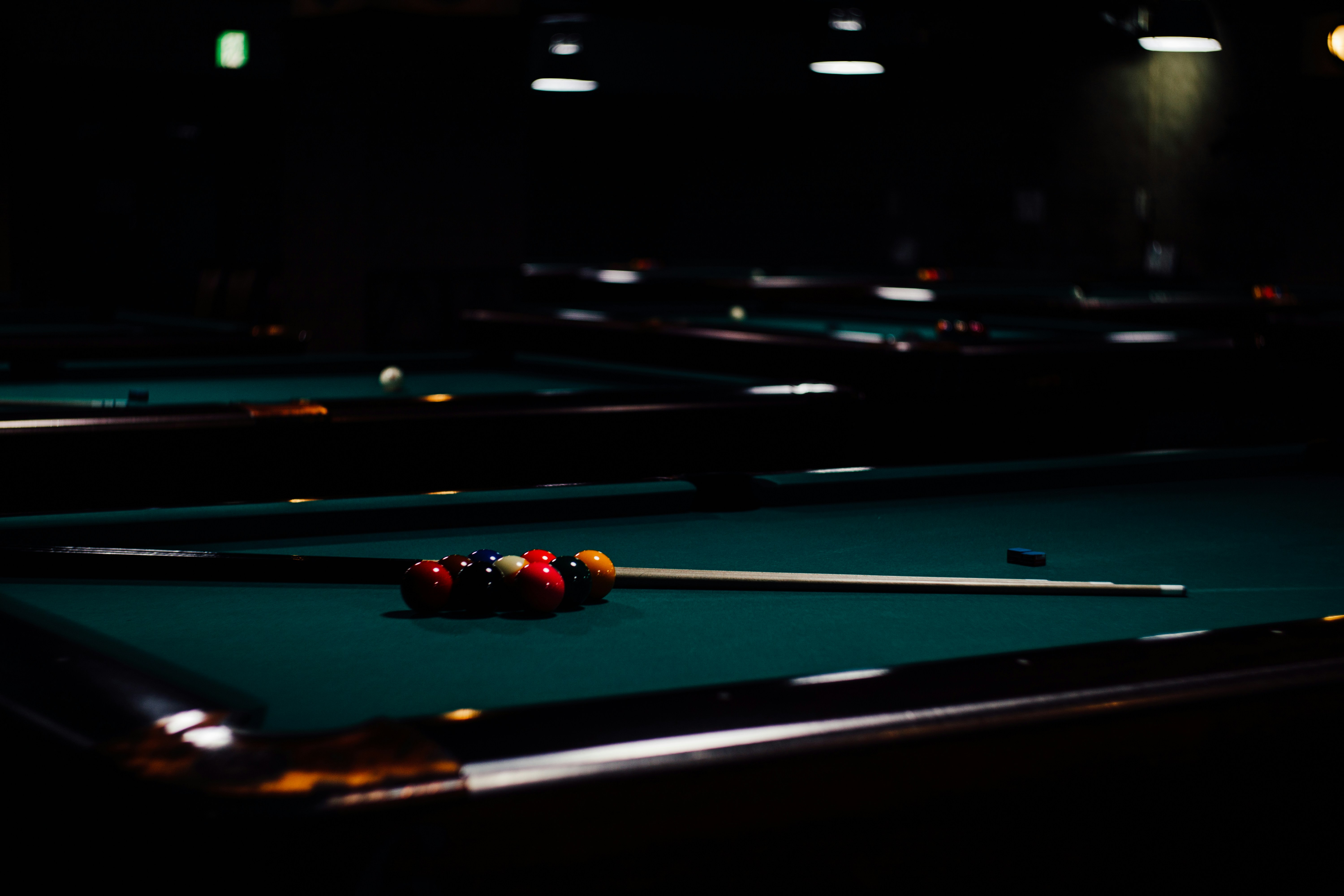 A dim billiard hall, balls racked under a low lamp